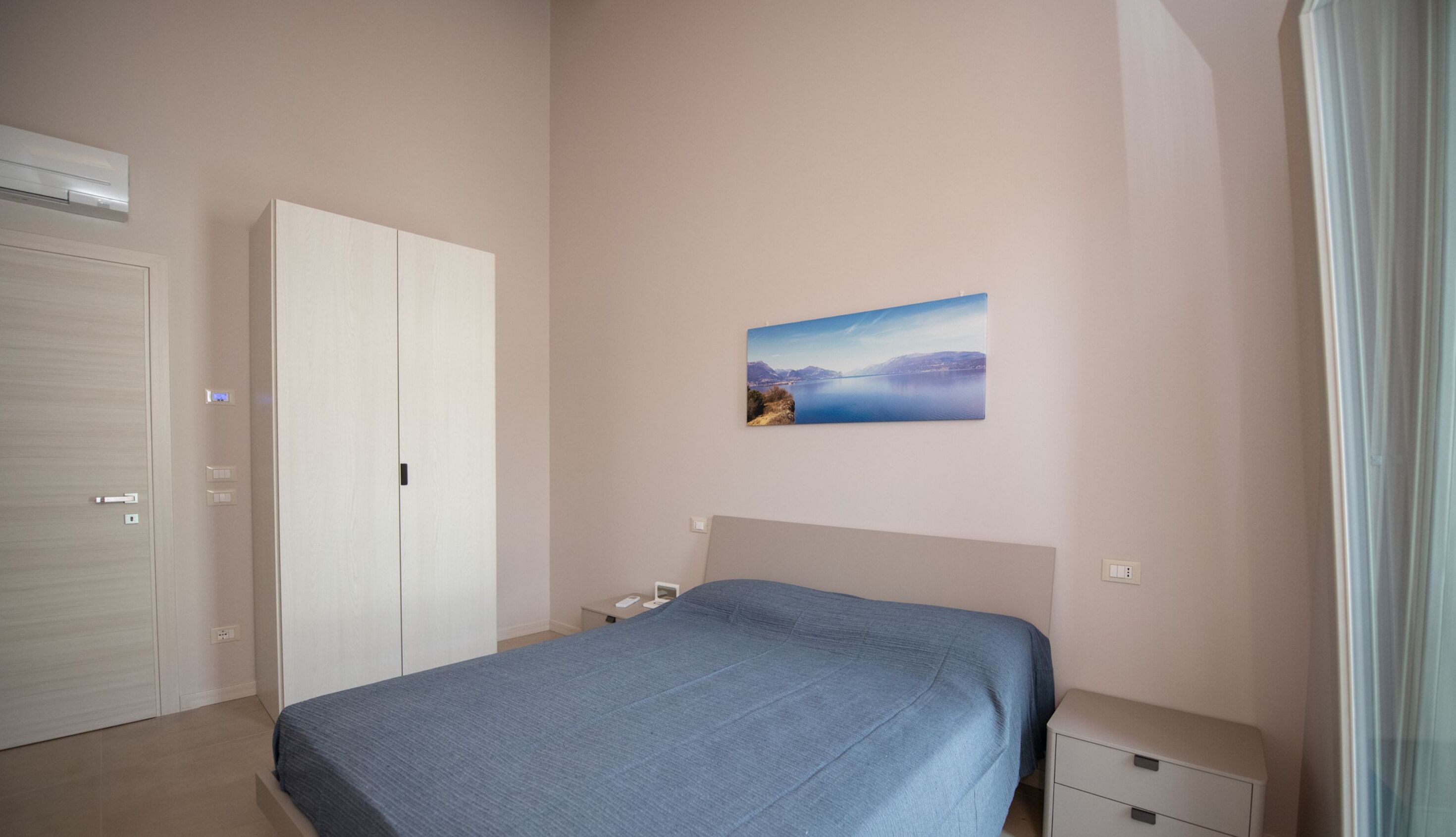 A bedroom with a bed, a wardrobe, a nightstand, and a painting on the wall.