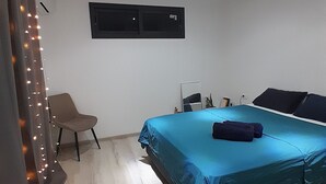 A bedroom with a bed, a chair, a desk, and a wall-mounted air conditioning unit.
