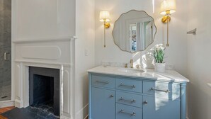 A bathroom with a marble sink, a blue vanity, a gold-framed mirror, and two wall-mounted lamps. - Beautifully Restored 3-Bedroom Home with Private Ensuite (Charleston)