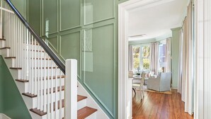 A staircase with white balusters and wooden steps leading to a room with a dining area and a view of greenery outside. - Beautifully Restored 3-Bedroom Home with Private Ensuite (Charleston)