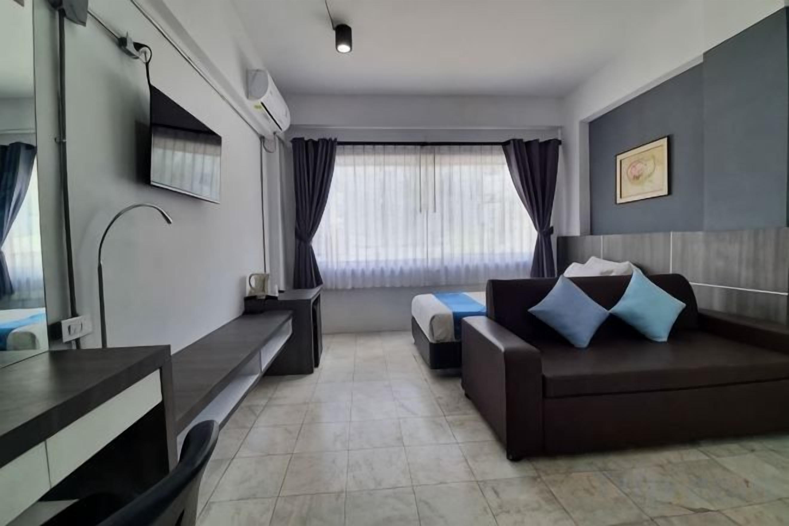 Habitación de hotel con cama, escritorio, silla, televisor y ventana con cortinas.