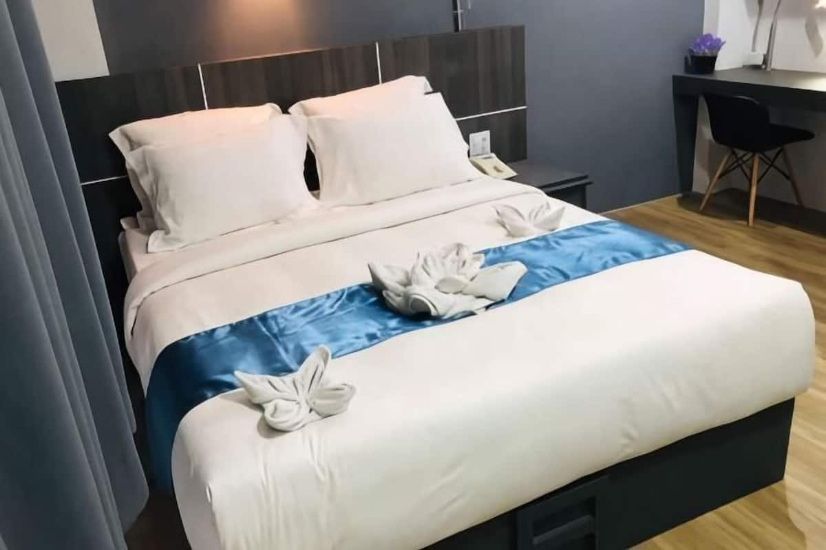 A neatly made bed with white linens and blue accents, a desk with a chair, and a nightstand.