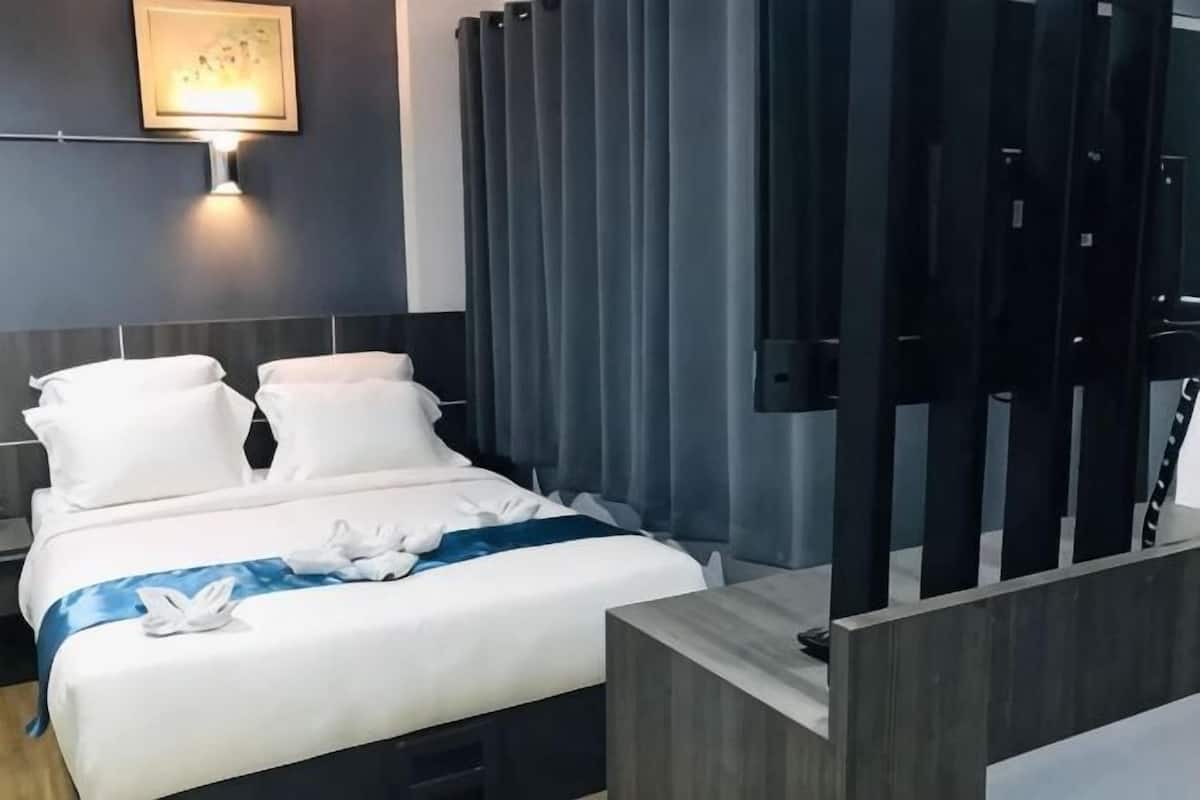 A modern hotel room with a bed, a nightstand, a wall-mounted lamp, and a curtain.