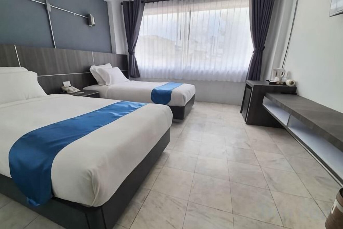 A hotel room with two beds, a desk, and a window with curtains.