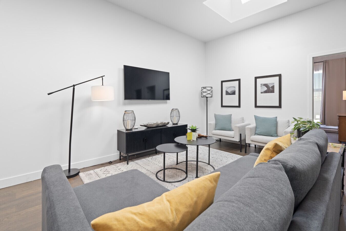 A modern living room with a grey sofa, a floor lamp, a black TV stand, and a small round table.