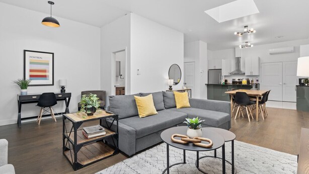 Un apartamento moderno con un sofá gris, una mesa de comedor, una cocina y una sala de estar con un ventanal grande.