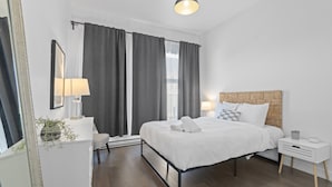 Un dormitorio moderno con cama, mesitas de noche, un espejo y una ventana con cortinas.