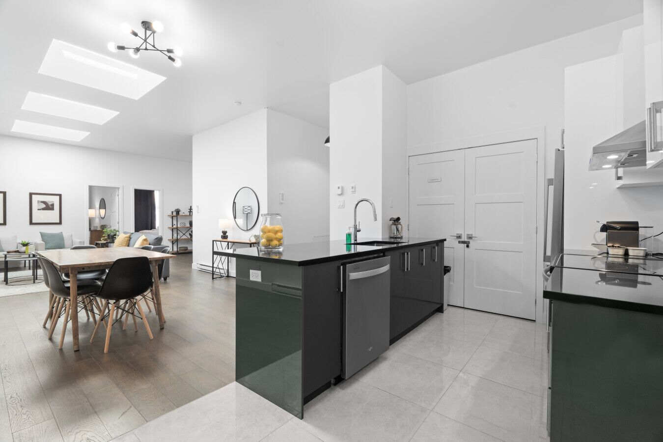 A modern kitchen with a central island, a dining area with a wooden table and chairs, and a living room with a sofa and a coffee table.