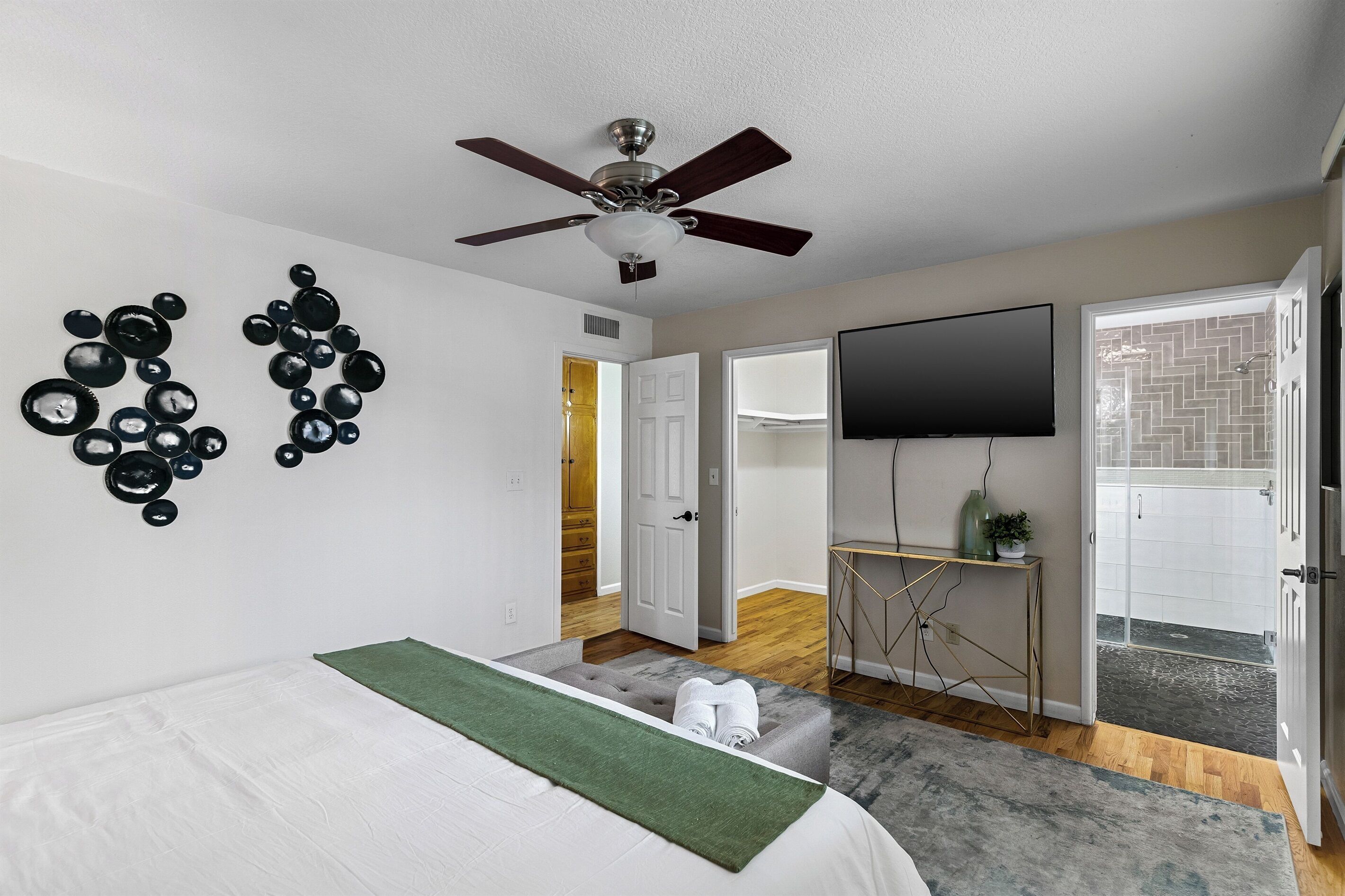 Une chambre à coucher comprenant un lit, un ventilateur de plafond, une télévision et une salle de bain avec douche.