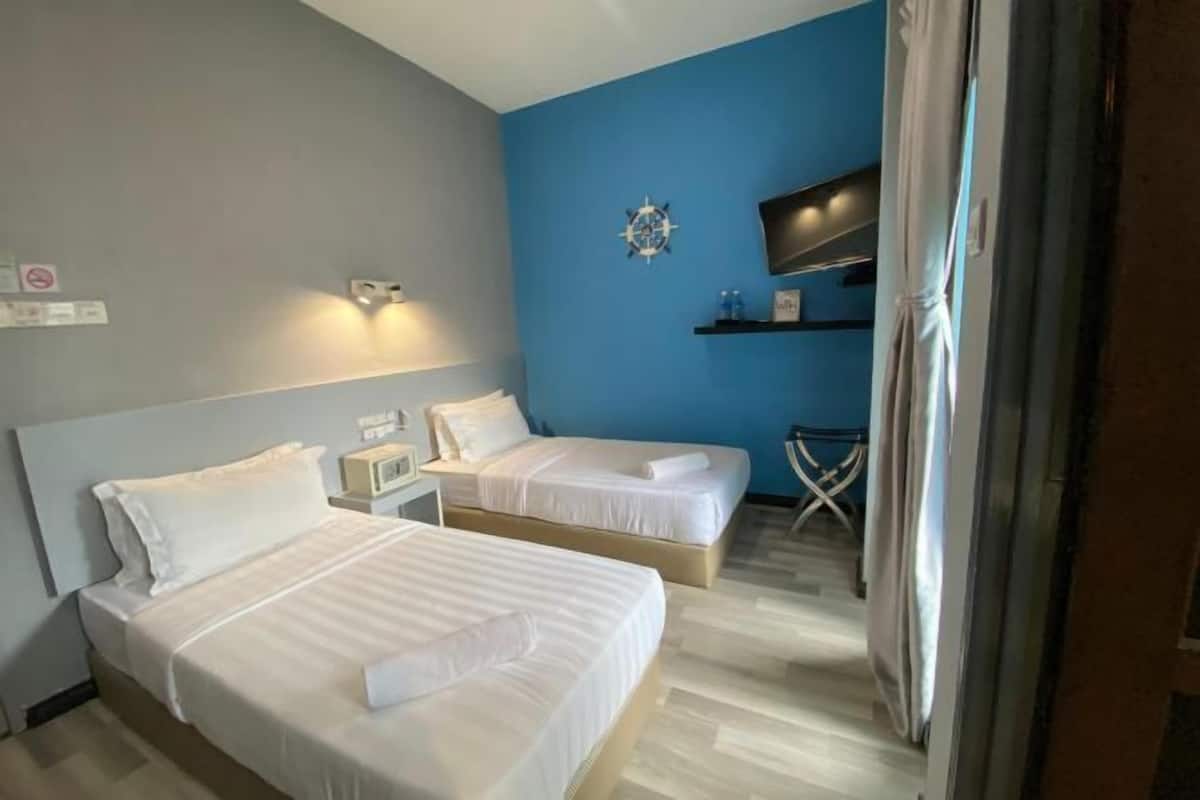 A hotel room with two beds, a TV, a clock, and a small table with a chair.