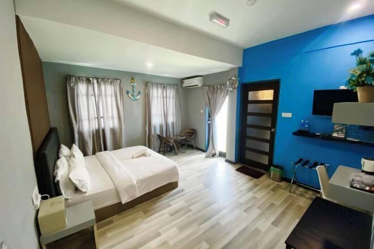 A hotel room with a bed, a desk, a chair, a TV, and a window with curtains.