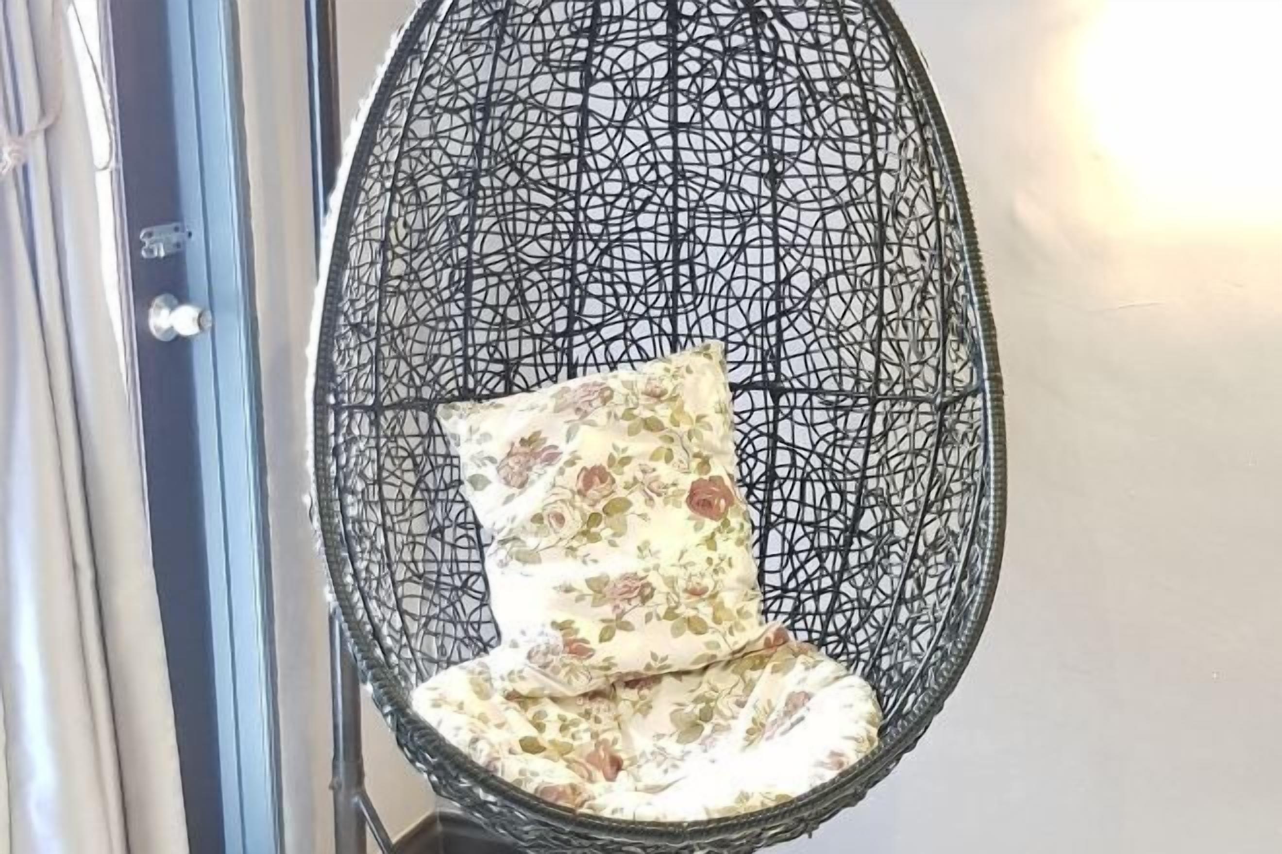 A hanging chair with a floral cushion in a room with a glass door and a wall-mounted light fixture.