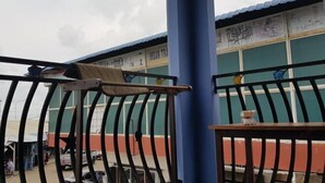 A metal railing with a towel hanging on it, a small table with a figurine, and a building with graffiti in the background. - Ang Lee Holiday Stay (Semporna)