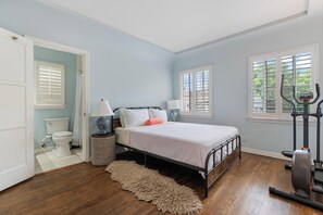 Ein Schlafzimmer mit einem Bett, Fitnessgeräten, einem Fenster mit Jalousien und einer Tür zu einem Badezimmer.