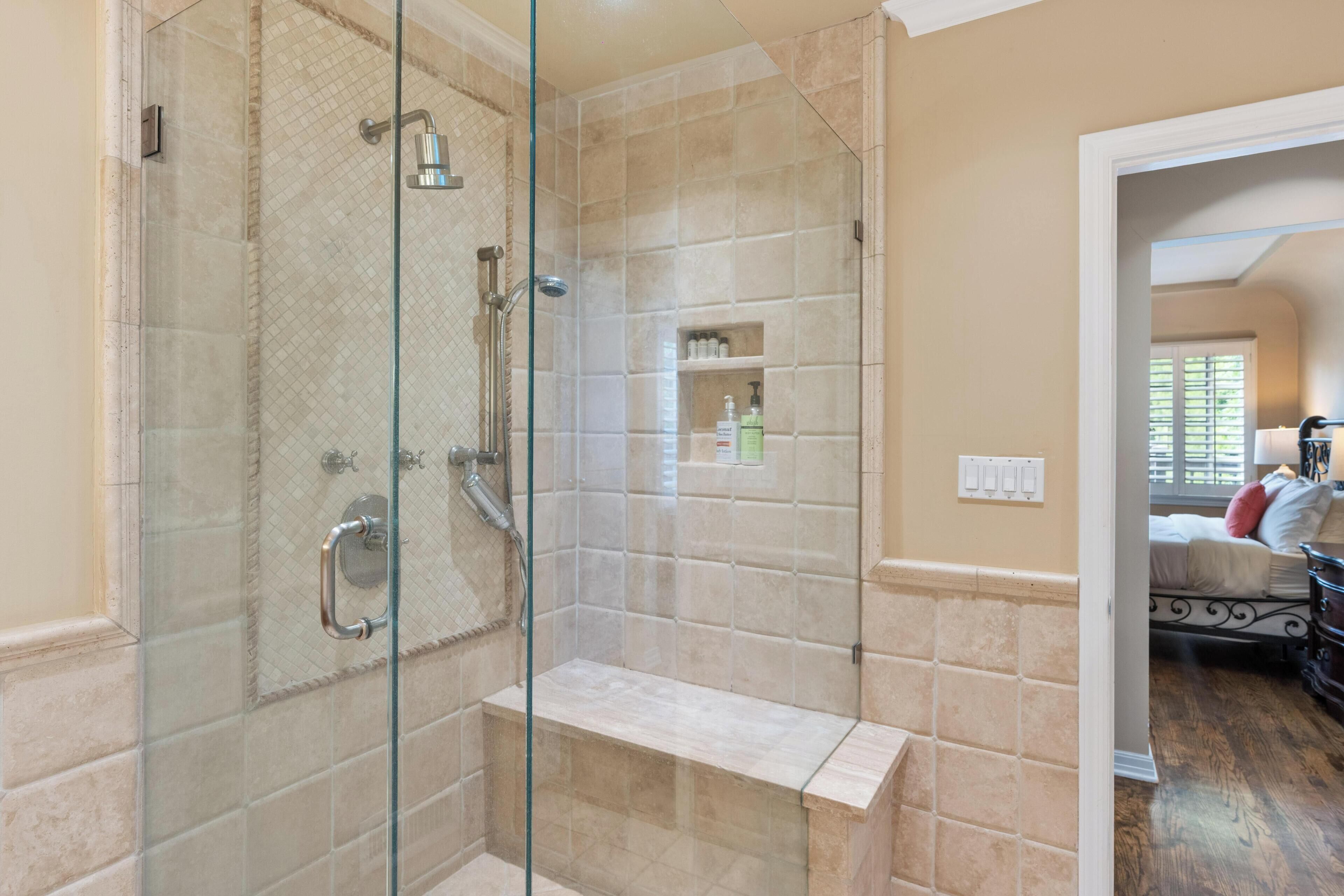 A modern bathroom with a glass-enclosed shower, beige tiles, and a built-in bench.