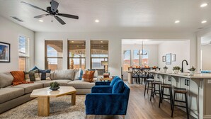 A modern living room with a sofa, blue armchairs, a coffee table, and a kitchen area with bar stools. - Crimson Ridge 1373, SLP 20, Private Pool, Game Room, Mountain Views, and Resort Access (Washington)