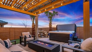 An outdoor patio with a fire feature, seating, a hot tub, and palm trees against a sunset backdrop. - Crimson Ridge 1373, SLP 20, Private Pool, Game Room, Mountain Views, and Resort Access (Washington)
