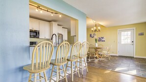 A dining area with wooden chairs and a table, a kitchen with white cabinets and appliances, and a yellow wall with artwork. - Shawano Lake House w/ Boat Dock, Kayaks, & Grill! (Cecil)