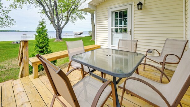 A wooden deck with a glass table and chairs, a small tree, and a view of a lake. - Shawano Lake House w/ Boat Dock, Kayaks, & Grill! (Cecil)