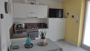 A compact kitchen with a microwave, toaster, and stove, a flat-screen TV, and a dining area with a table and chairs. - BLONDIE HOUSE (Fonteno)
