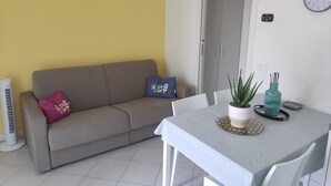 A living room with a sofa, a dining table, a potted plant, and a wall clock. - BLONDIE HOUSE (Fonteno)