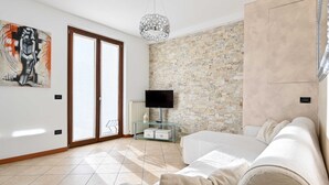Un salon moderne avec un canapé, un téléviseur posé sur un meuble en verre, un mur en pierre et une porte avec des panneaux de verre.