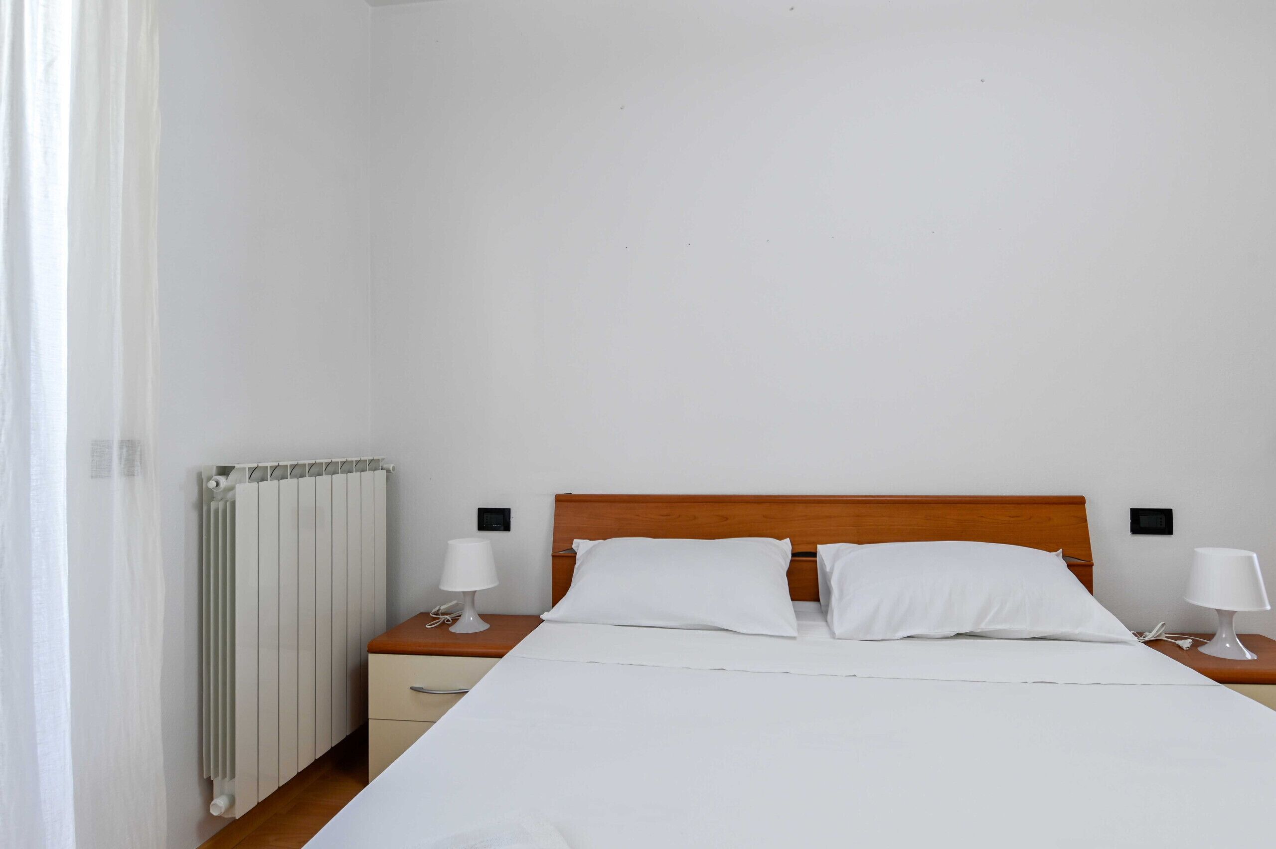 Un lit bien fait, avec du linge de lit blanc, une tête de lit en bois et deux lampes de chevet.