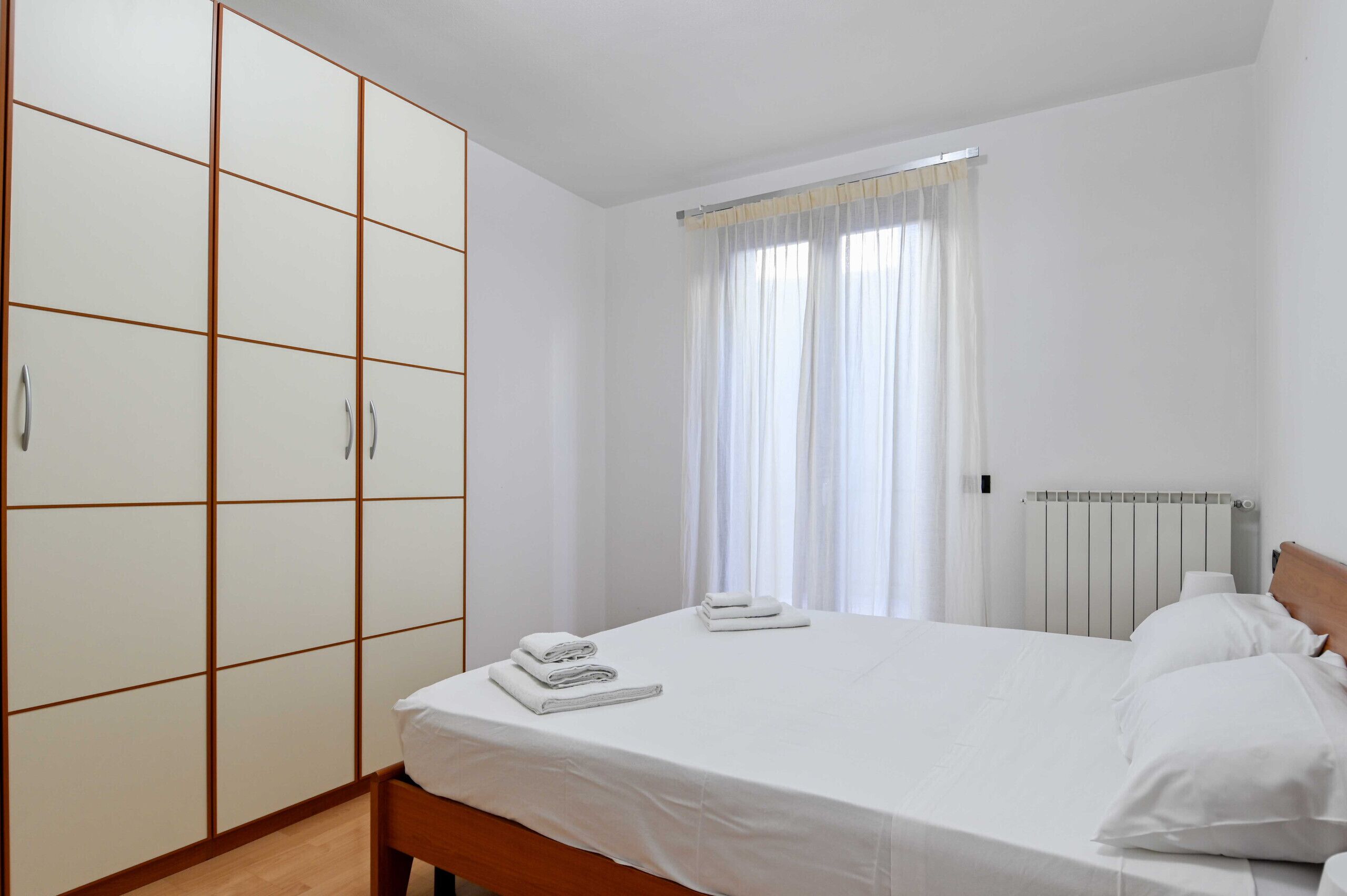 Ein Schlafzimmer mit einem Bett, einem Kleiderschrank und einem Fenster mit Vorhängen.