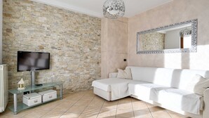 Un salon moderne avec un mur en pierre, un canapé blanc, une table basse en verre, un téléviseur à écran plat et un luminaire décoratif.
