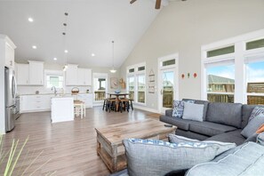 Un espacio habitable amplio con un sofá gris, una mesa de centro de madera, y una cocina con armarios blancos y una zona de comedor.