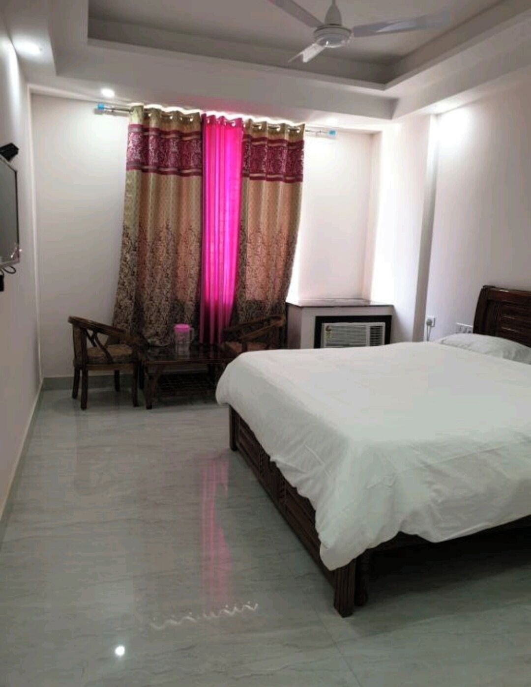 A bedroom with a bed, a desk with a chair, a television, and a ceiling fan.