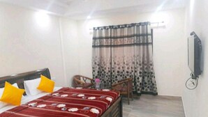 A hotel room with a bed, two chairs, a TV, and a window with curtains. - Hotel The Ganga Castle (Haridwar)