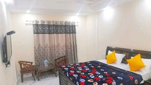 A bedroom with a bed, two chairs, a table, a curtain, and a wall-mounted phone. - Hotel The Ganga Castle (Haridwar)