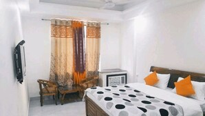 A bedroom with a bed, two chairs, a small table, and a heater. - Hotel The Ganga Castle (Haridwar)