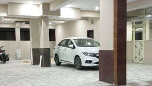 A covered parking area with a white car parked inside, checkered floor tiles, and a column structure. - Hotel The Ganga Castle (Haridwar)
