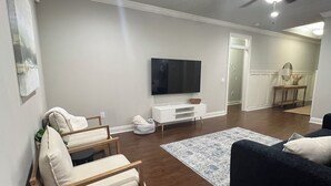A modern living room with a dark blue sofa, a wooden bench with cushions, a flat-screen TV, and a white entertainment unit. - Charming 3-bedroom house with WiFi, AC in fabulous Navarre Beach 7 min away. (Navarre)