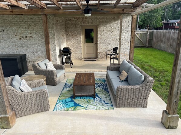Relax in a shaded outdoor space with a seating area, coffee table, and grill, surrounded by a grassy yard.