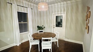 A dining area with a round wooden table surrounded by white chairs, a hanging woven light fixture, and a potted plant. - Charming 3-bedroom house with WiFi, AC in fabulous Navarre Beach 7 min away. (Navarre)