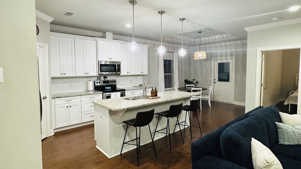 A modern kitchen with white cabinets, a central island with bar stools, and pendant lighting. - Charming 3-bedroom house with WiFi, AC in fabulous Navarre Beach 7 min away. (Navarre)