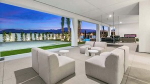 A modern outdoor lounge area with a pool, white furniture, and a view of mountains. - Private Estate-Waterslide-Theatre-Sauna-Pickleball (Indio)