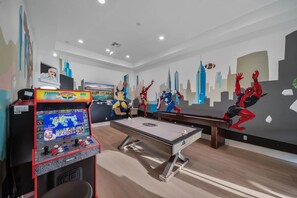 A room with a foosball table, a pool table, and a large mural of superheroes.