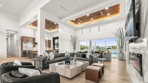 A spacious living area with a modern kitchen, a fireplace, and large windows offering a view of the outdoors. - Private Estate-Waterslide-Theatre-Sauna-Pickleball (Indio)