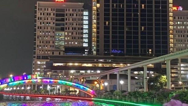 A brightly lit bridge with colorful lights, a modern building with "AIA" sign, and a pedestrian walkway. - The Pines by Amanjiwa (Melaka)
