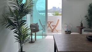 A modern living room with a large potted plant, a wooden dining table, and a view of a balcony with outdoor furniture. - Private Island 1BR Condo with Oceanview, Pool View, 500MB WiFi & A/C (Fajardo)