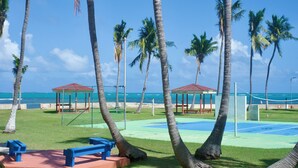 A tennis court with palm trees, benches, and gazebos. - Private Island 1BR Condo with Oceanview, Pool View, 500MB WiFi & A/C (Fajardo)