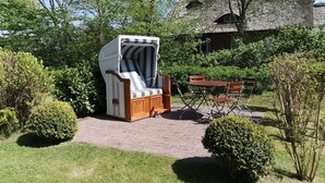 Un jardin agrémenté d’un fauteuil de relaxation en osier, d’un banc en bois et d’un bâtiment à toit de chaume.