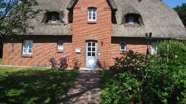 Une maison traditionnelle en briques, avec un toit de chaume, une entrée centrale et un petit porche.