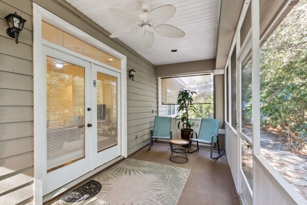 A covered porch with two chairs, a potted plant, and a ceiling fan. - Summer Beach House - Hosted by Moore AI Rentals (Fernandina Beach)