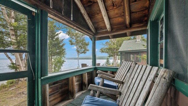 Une véranda en bois avec un banc, d’où l’on a vue sur un lac et une maison.
