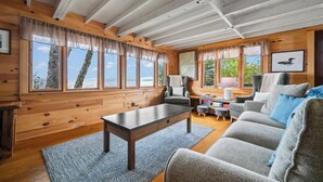 L’intérieur d’un chalet accueillant, avec un plafond en bois, de grandes fenêtres, un canapé, une table et une chaise.